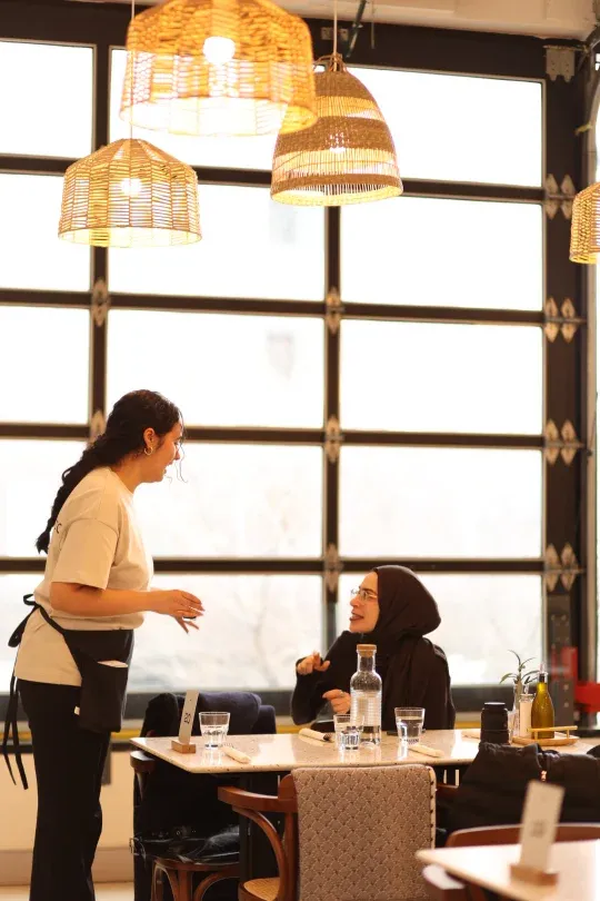 Server chatting with a guest at a sunlit window table at Eggstatic