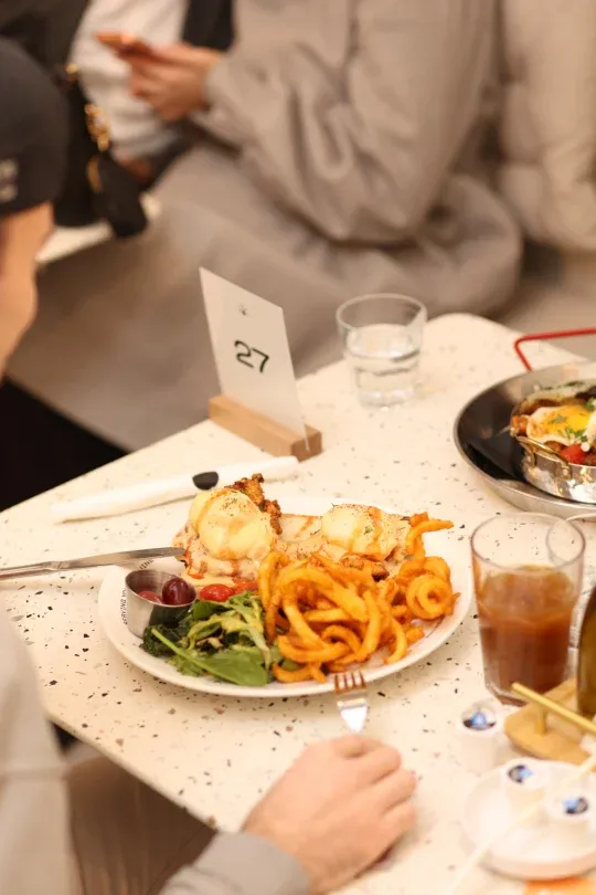 Eggs benedict with curly fries and side salad on a terrazzo table at Eggstatic