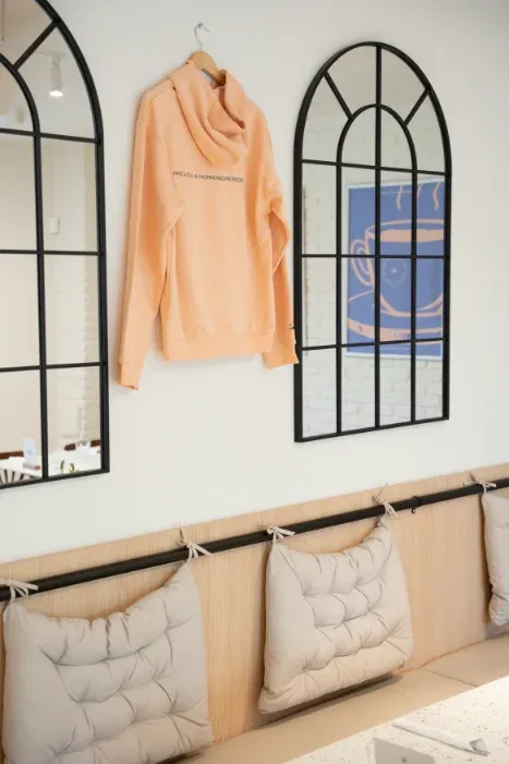 Peach "Proudly a Morning Person" hoodie between arched windows with coffee artwork at Eggstatic London Ontario