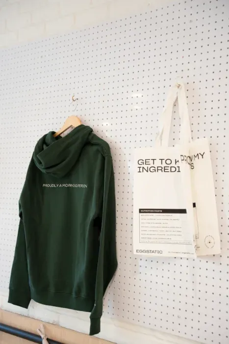 Green Eggstatic hoodie and "Get to know my ingredients" tote on the merch pegboard at Eggstatic London Ontario