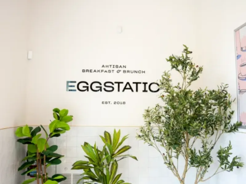Eggstatic "Artisan Breakfast & Brunch — Est. 2018" entry wall and large plants at the London Ontario location