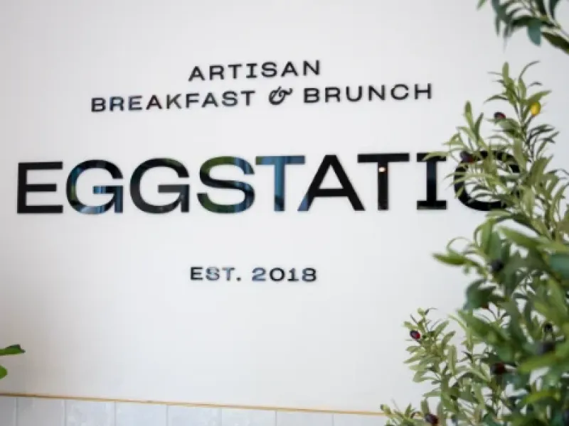 Eggstatic "Artisan Breakfast & Brunch — Est. 2018" wall sign with olive plant at Eggstatic London Ontario